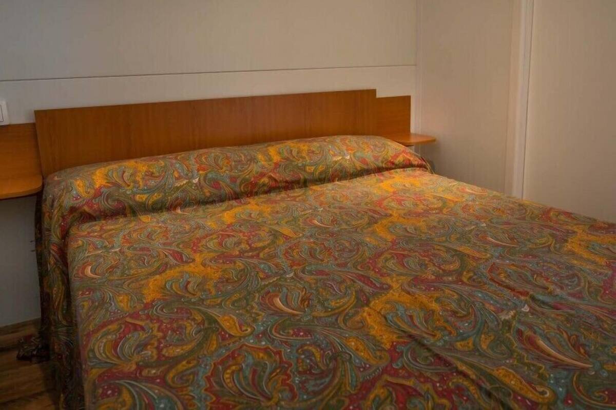Een slaapkamer met een houten hoofdbord, een kleurrijk beddegoed met dessin en een klein nachtkastje.