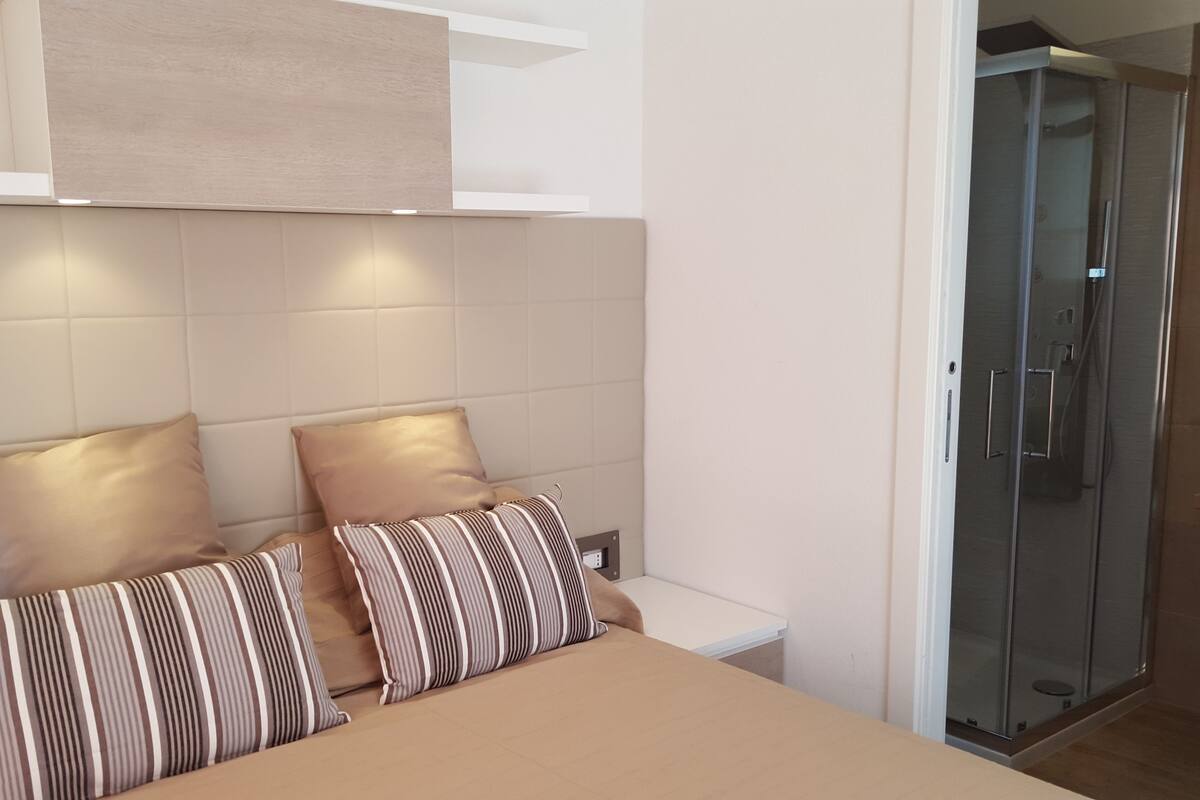 Een moderne slaapkamer met een bed, twee kussens, een nachtkastje en een inloopkast.