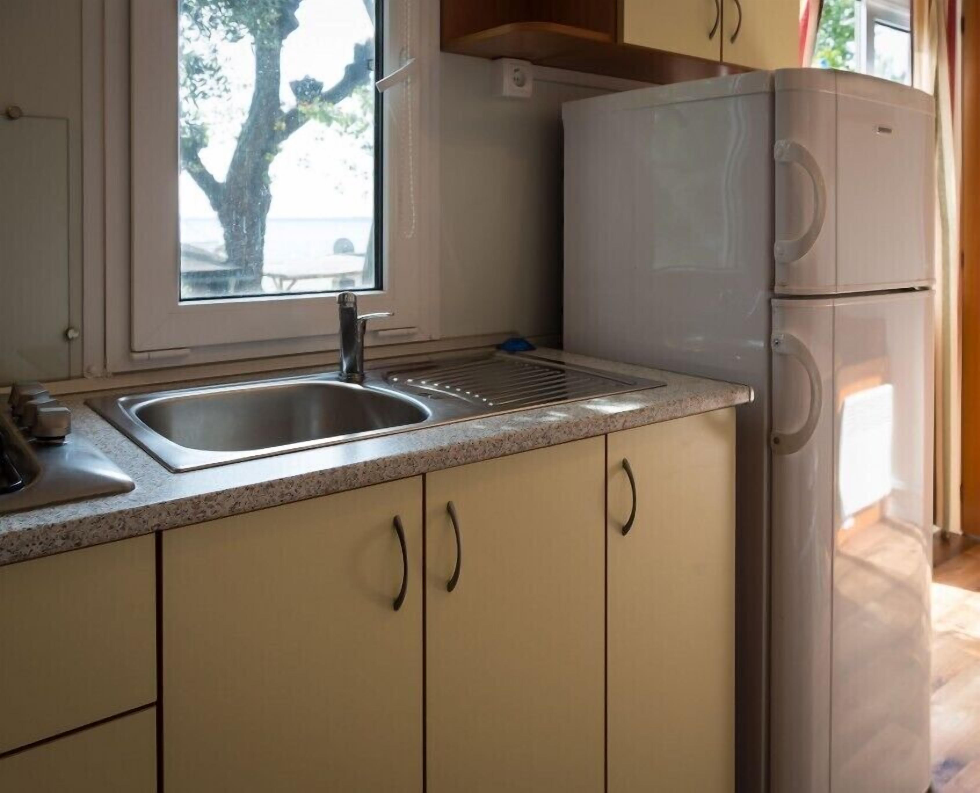 A kitchen with a stainless steel sink, a window, and a white refrigerator.