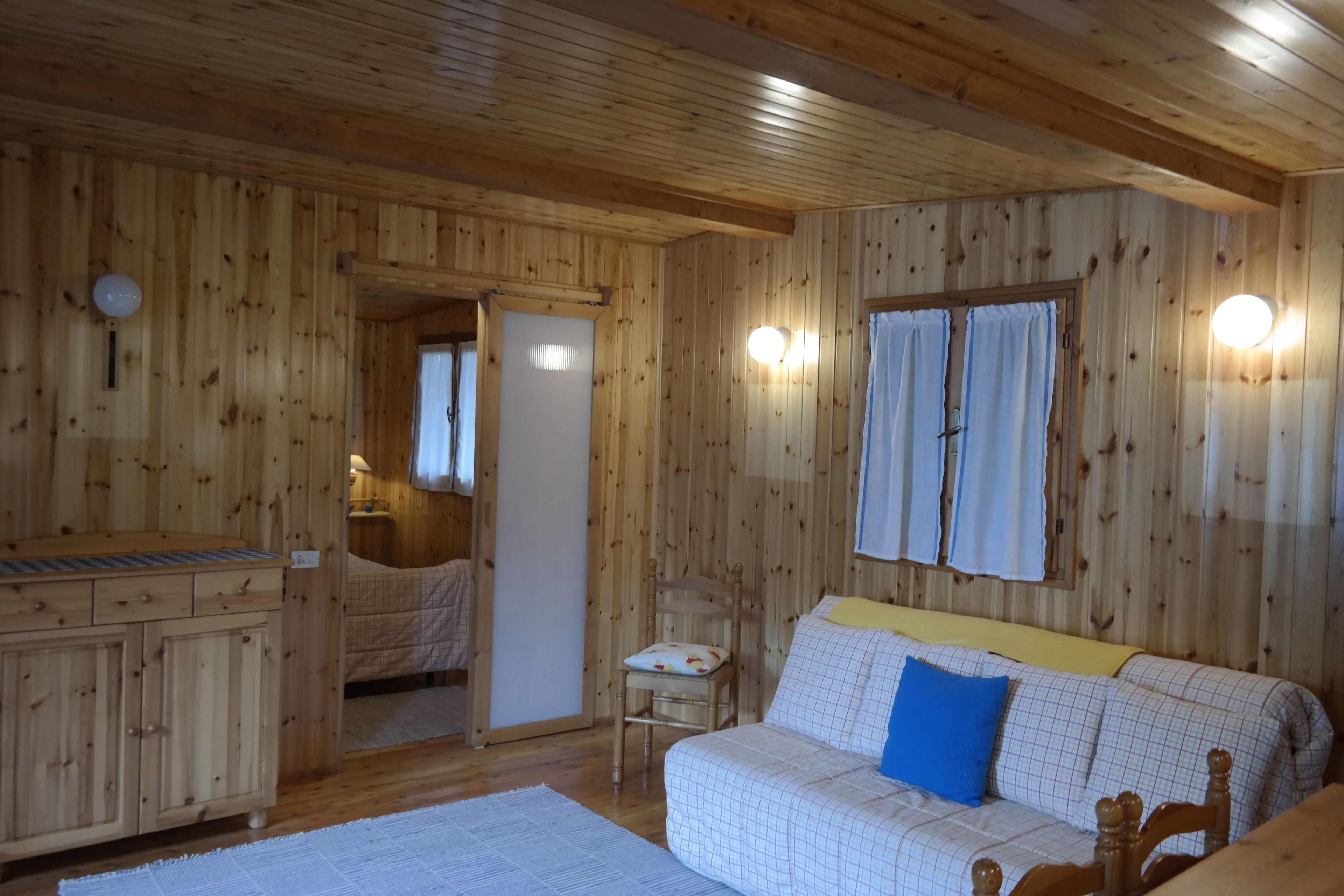 A wooden cabin interior with a bed, a sofa, a wooden cabinet, and a small table.