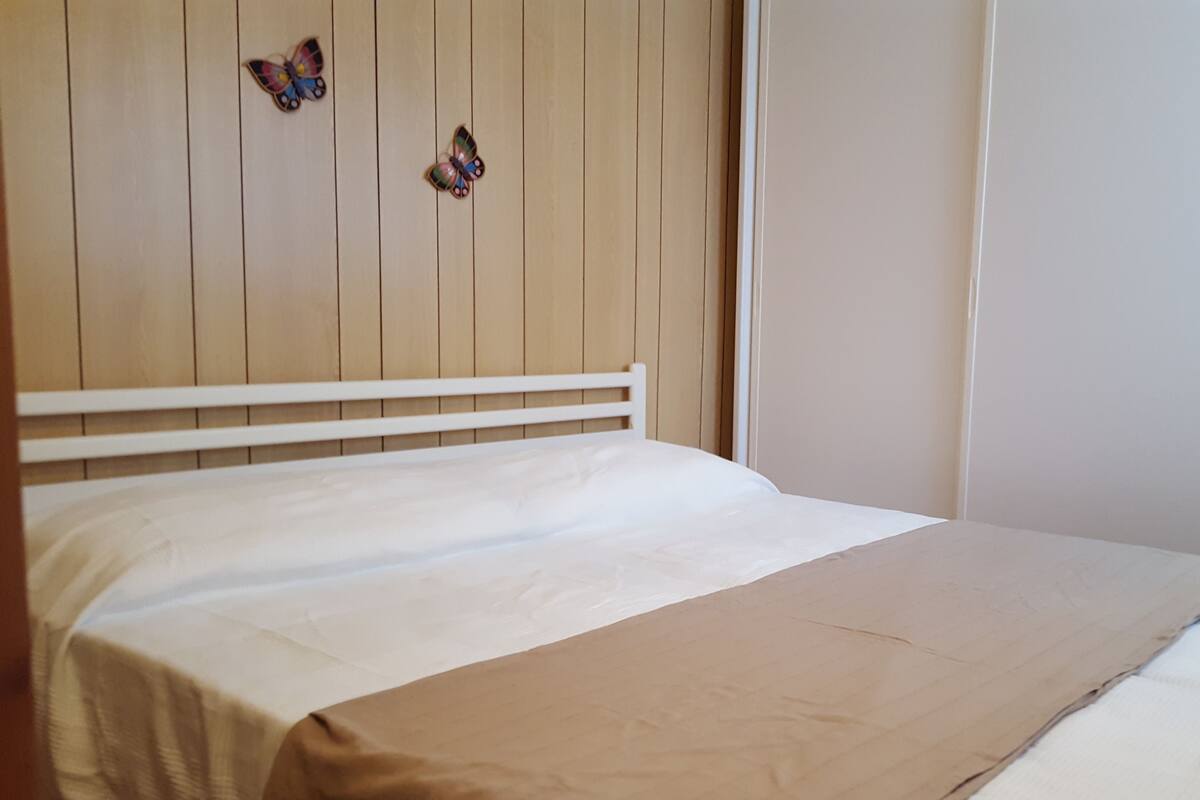 Een bed met een houten hoofdbord, een wit matras en een beige sprei.