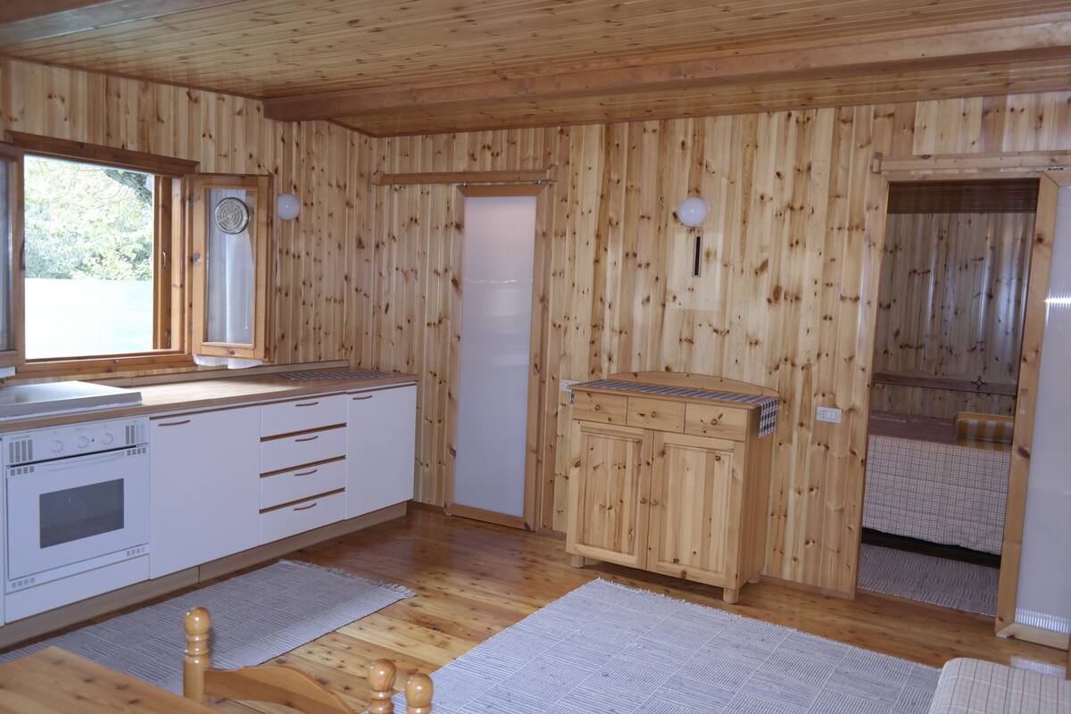Een houten hut met een keukenhoek, inclusief een kookplaat, koelkast en houten kastjes.