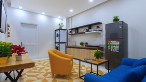Cocina moderna con refrigerador, lavaplatos y armarios de madera. Hay una mesa de comedor con sillas y un sofá azul.