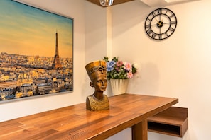 A wooden table with a decorative bust, a wall clock, a framed cityscape painting, and a vase with flowers. - Taksim Yazici Residence (Istanbul)