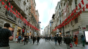 Une rue animée en milieu urbain, avec des voies de tramway, des piétons et des immeubles ornés de drapeaux rouges.
