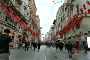 A busy urban street with tram tracks, pedestrians, and buildings with red flags. - Taksim Yazici Residence (Istanbul)