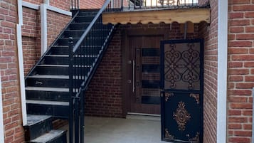 Um corredor estreito ao ar livre com uma escadaria de metal que leva a uma porta de madeira com painéis decorativos.