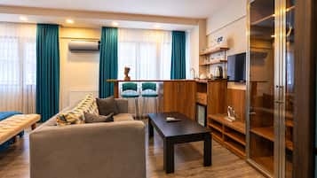 Uma sala de estar moderna com sofá, mesa de centro e área de jantar com cadeiras. Há uma TV em um armário de madeira, e um guarda-roupa com portas de vidro.