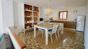 Eine kleine Küche mit einem Holztisch, weißen Stühlen und einer Einbauküche mit Geschirr.