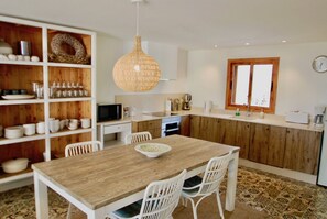 Une cuisine moderne avec des meubles blancs, une table à manger en bois et un luminaire suspendu.