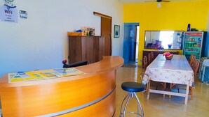 Una recepción con mostrador de madera, una mesa de comedor con sillas y un refrigerador lleno de bebidas.