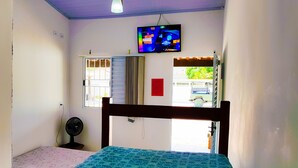 Un dormitorio con cama, ventilador de techo, televisor en la pared y ventana con vista al exterior.