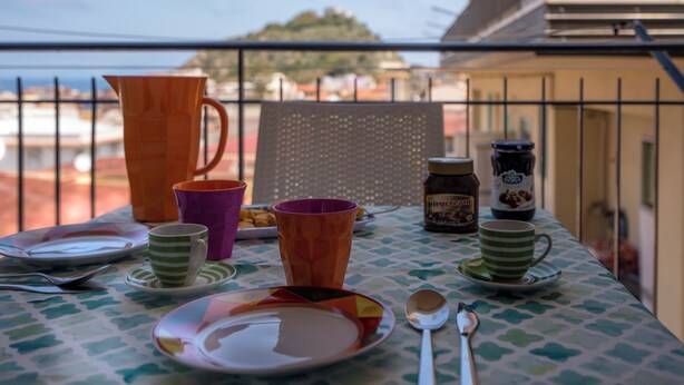 Ein Balkontisch gedeckt mit Tellern, Tassen, einer Karaffe und einem Marmeladenglas.