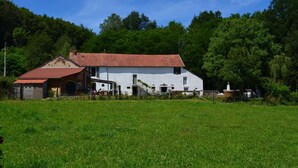 A white farmhouse with a red roof, surrounded by a green field and trees.
