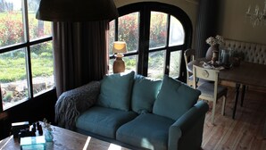 A cozy living room with a large window, a wooden dining table, and a blue sofa.