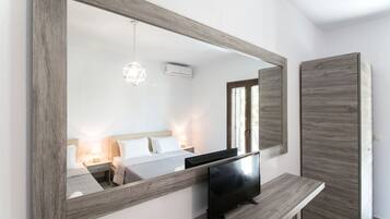 Quarto com um espelho grande, televisão, mesa de cabeceira, cama e janela.