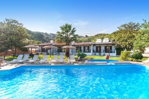 Une piscine avec des chaises longues, un palmier et un bâtiment doté d’un toit en tuiles.