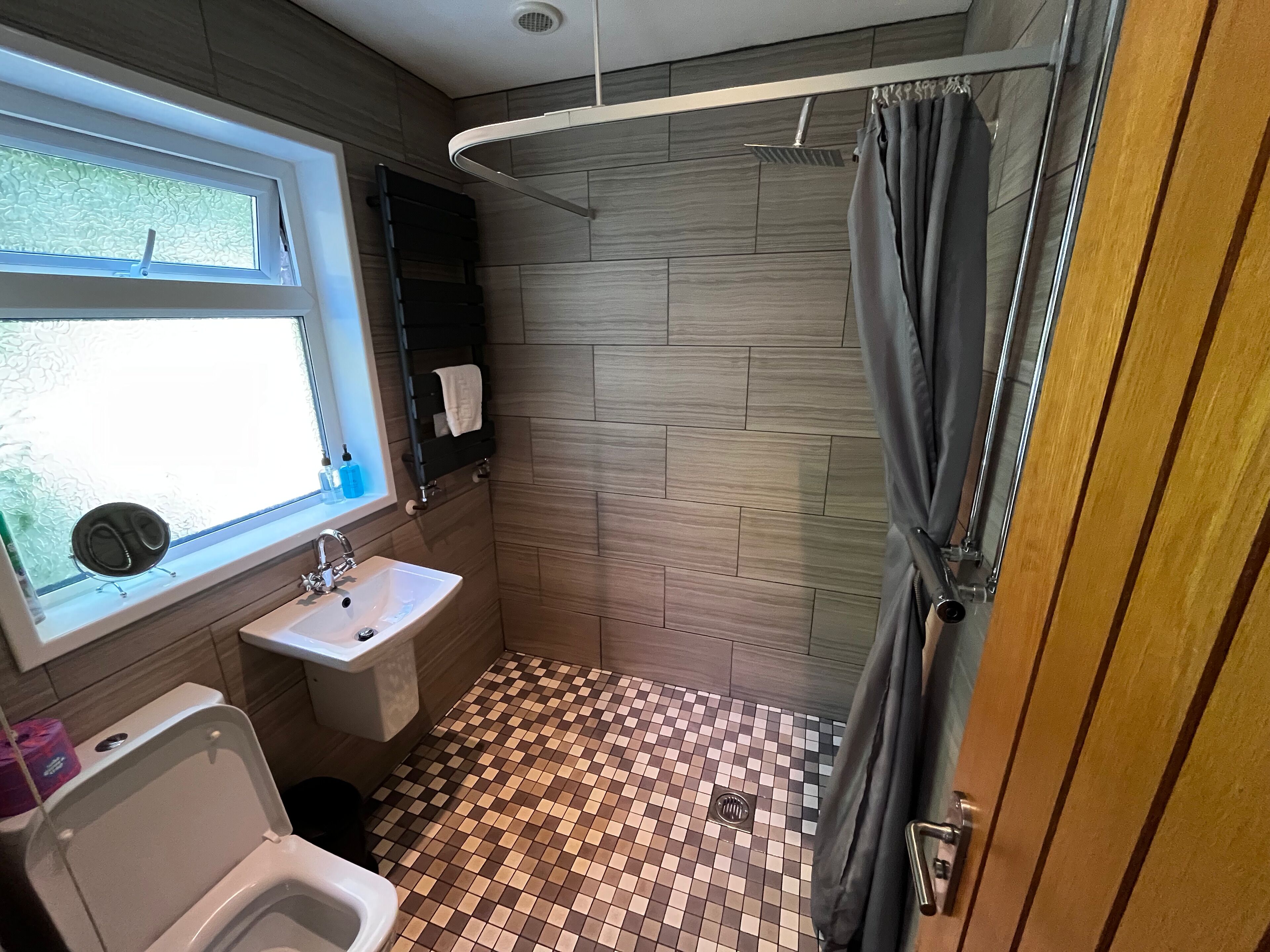 Un baño con piso a cuadros, un lavamanos, un inodoro, una ventana y una cortina de ducha.