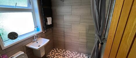 Un baño con piso a cuadros, un lavamanos, un inodoro, una ventana y una cortina de ducha.