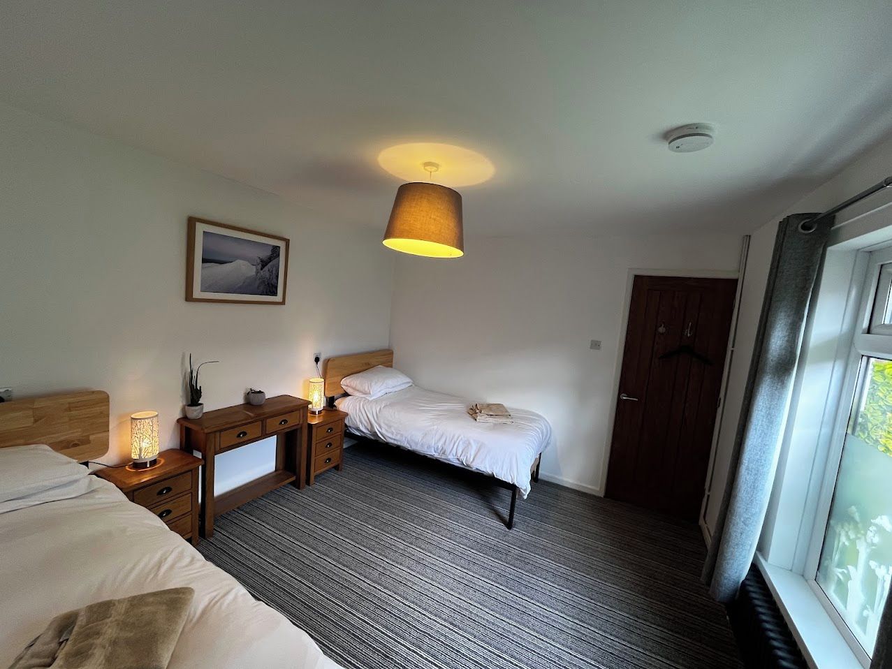 A hotel room with a bed, bedside table, lamp, and a window with curtains.