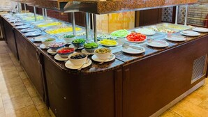 Un mostrador de buffet con diversos alimentos en boles y fuentes, como ensaladas, frutas y verduras.
