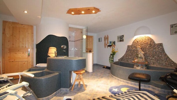 A spa area with a stone hot tub, wooden stools, and a stone wall with a statue. - Schmuckenhof (Marktschellenberg)