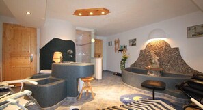 Un espace de détente avec un bain à remous en pierre, des tabourets en bois et un mur de pierre orné d’une statue.