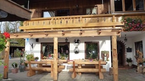 A wooden pergola with benches, a white building with a balcony, and hanging flower baskets. - Schmuckenhof (Marktschellenberg)