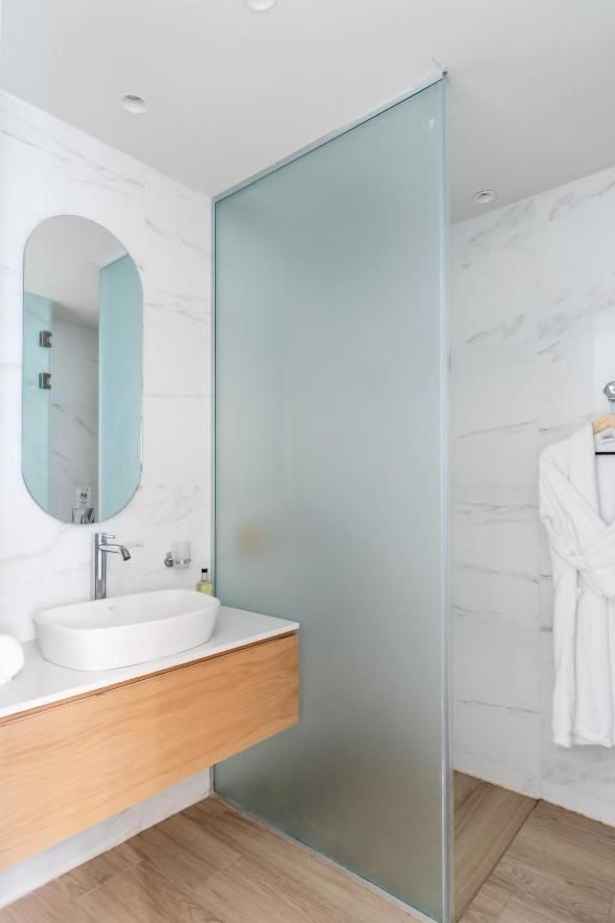 Un baño moderno con cabina de ducha de vidrio, tocador de madera y pared con azulejos de mármol.