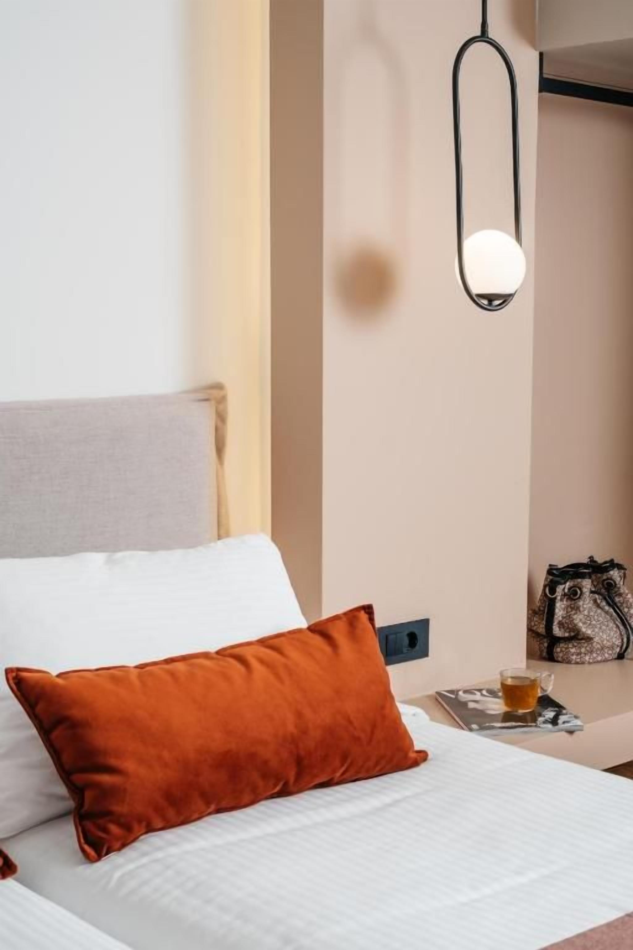 Una habitación de hotel con una cama, una mesita de noche con una lámpara, un bolso y una taza.