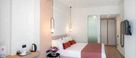Una habitación de hotel moderna con una cama grande, una mesita de noche con hervidor, una pequeña mesa con flores y un televisor montado en la pared.