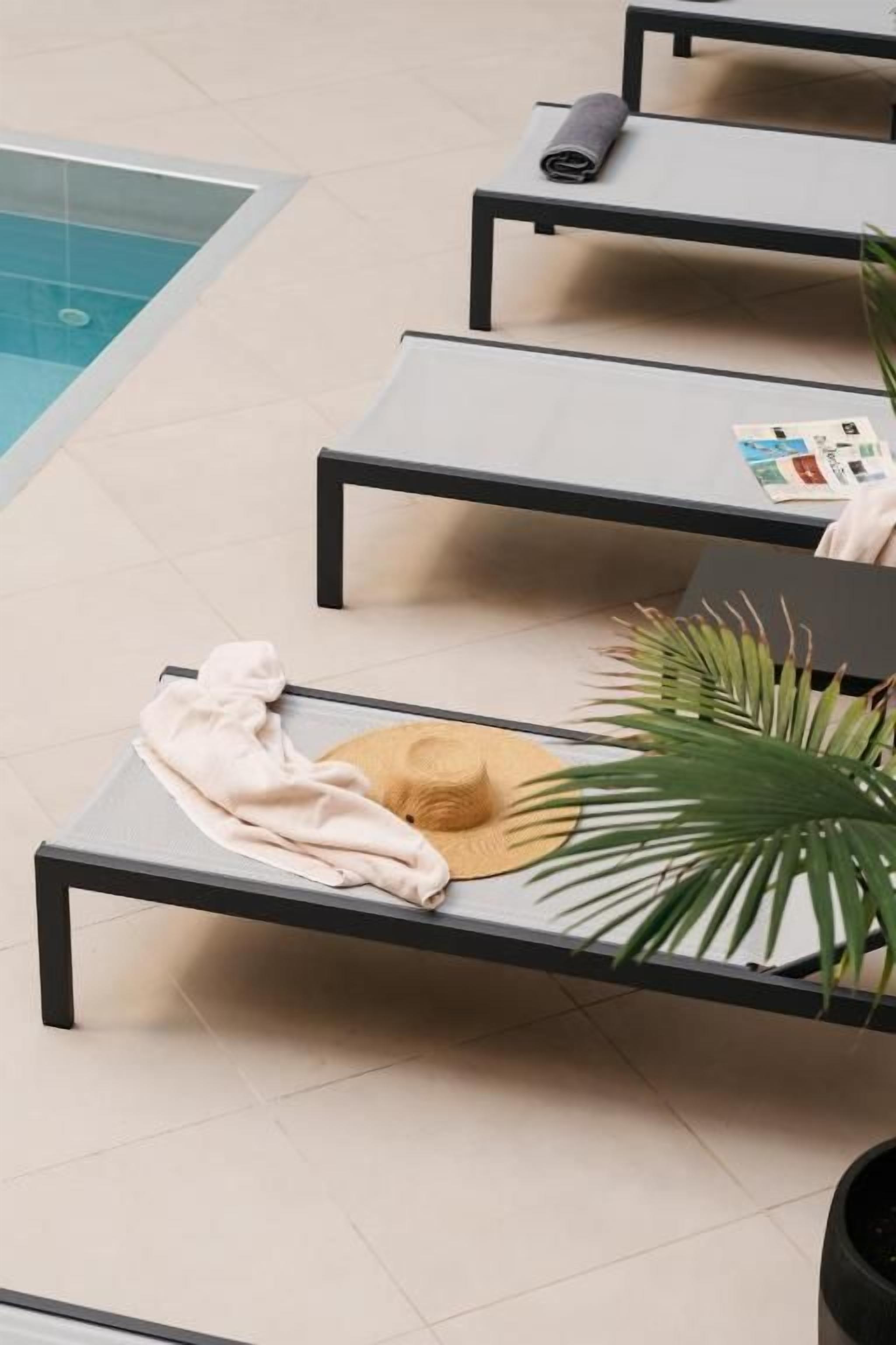 A poolside lounge area with sun loungers, a pool, and a potted plant.