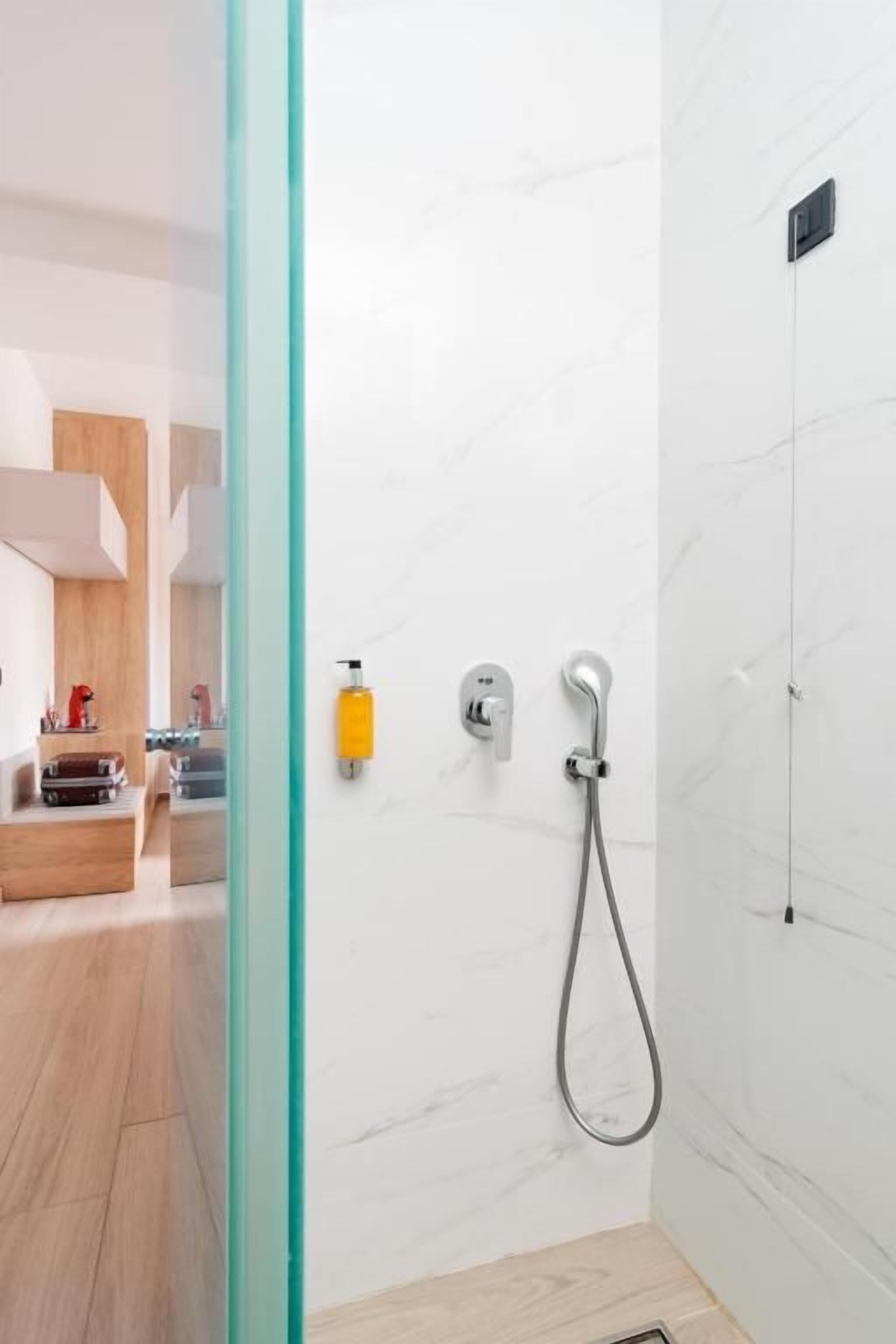 A modern bathroom with a glass shower enclosure, a handheld showerhead, and a wall-mounted faucet.