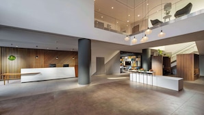 A spacious lobby with a reception desk, seating area, and a staircase leading to upper floors. - Clarion Hotel Vienna South (Vienna)