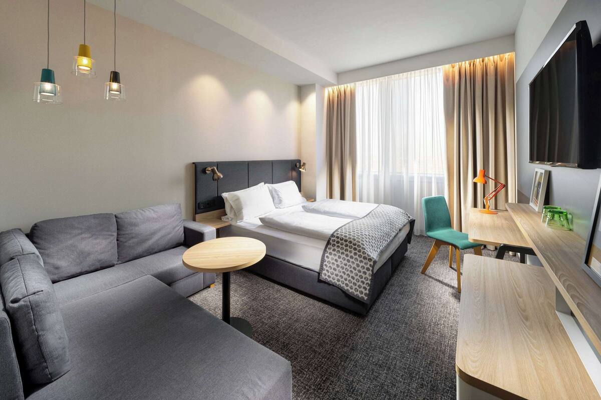 Una habitación de hotel moderna con cama, sofá, escritorio y televisor.