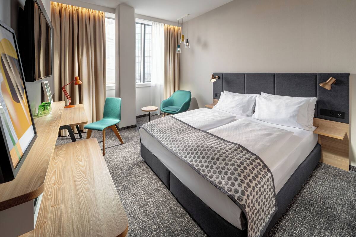 Una habitación de hotel con una cama grande, un escritorio con silla, un televisor y una ventana con cortinas.