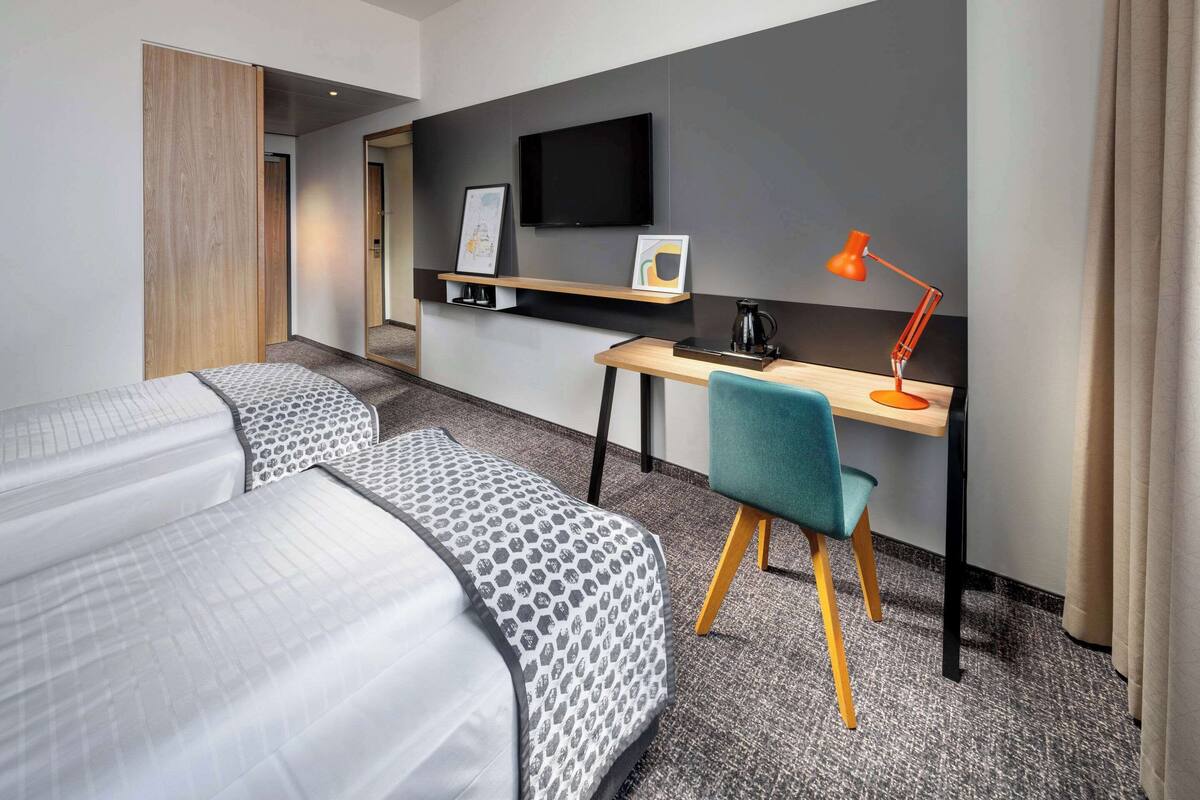Habitación de hotel con dos camas, un escritorio, una silla, un televisor y una cafetera.