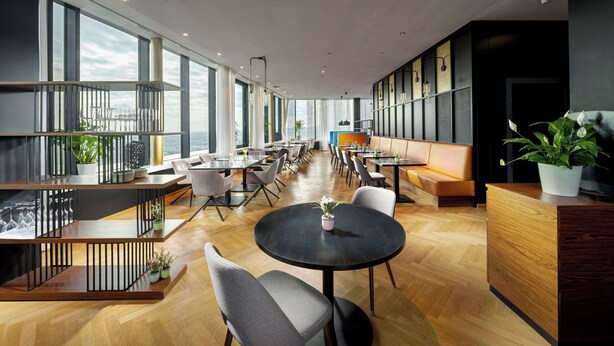 A modern hotel lobby with a long dining area, multiple tables, and a reception desk. - Clarion Hotel Vienna South (Vienna)