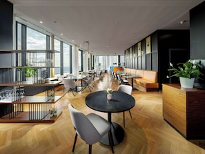 Um lobby de hotel moderno com uma extensa área de jantar, diversas mesas e um balcão de recepção.