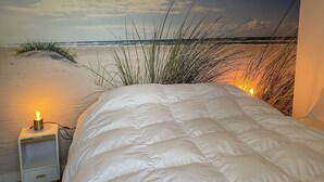 A bedroom with a beach mural on the wall, a white bed, and a bedside lamp. - Bungelow "Duinvogel" Beach with bath in the garden (Noordwijk)