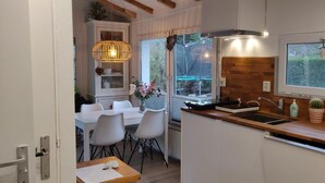 A compact kitchen with white cabinetry, a wooden countertop, a built-in sink, and a window overlooking a garden. - Bungelow "Duinvogel" Beach with bath in the garden (Noordwijk)