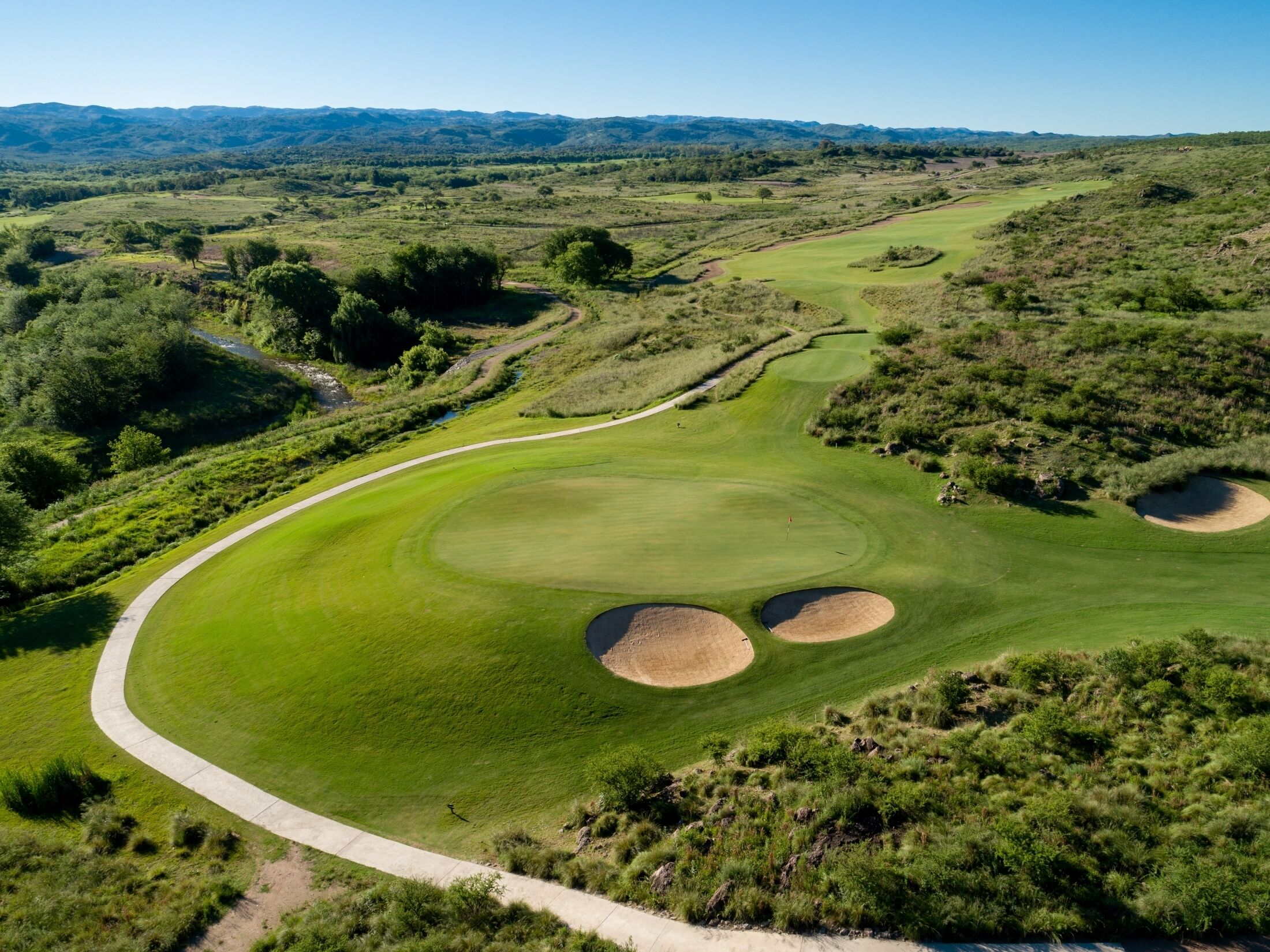 Un parcours de golf avec un chemin sinueux, des bunkers de sable et un paysage vallonné en arrière-plan.