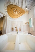 Un baño con dos lavamanos, una lámpara de techo trenzada grande y paneles de pared de madera.