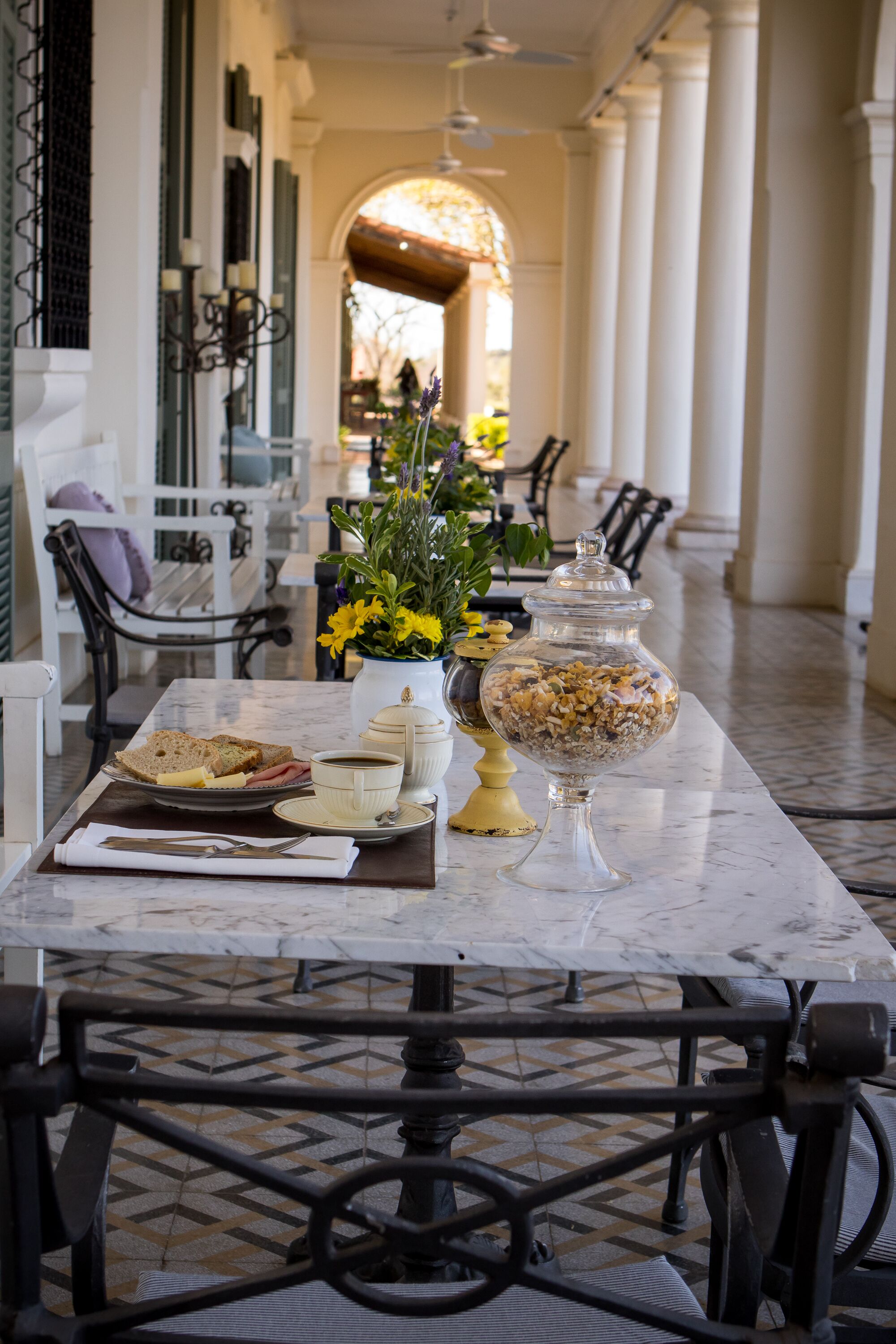 Une table surmontée d’un plateau en marbre, avec des aliments pour le petit-déjeuner, un vase de fleurs et un pot décoratif.