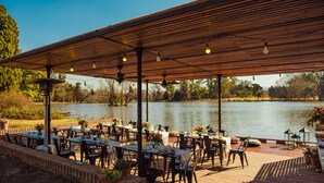 Un espace extérieur aménagé pour les repas, avec des tables et des chaises, une pergola en bois et une vue sur un lac.