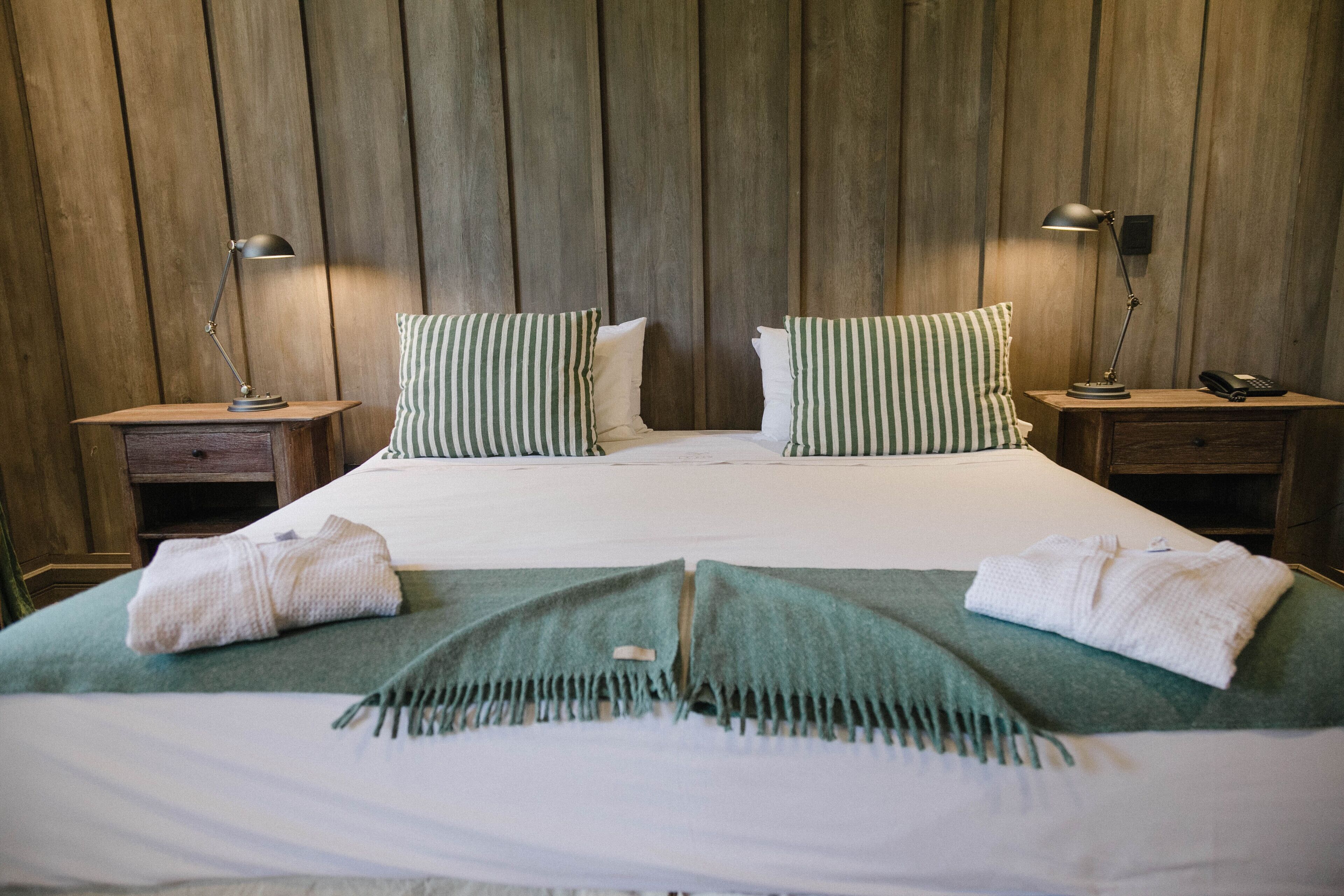 Una camera d'albergo con un letto grande, due comodini, una testiera in legno e due lampade.