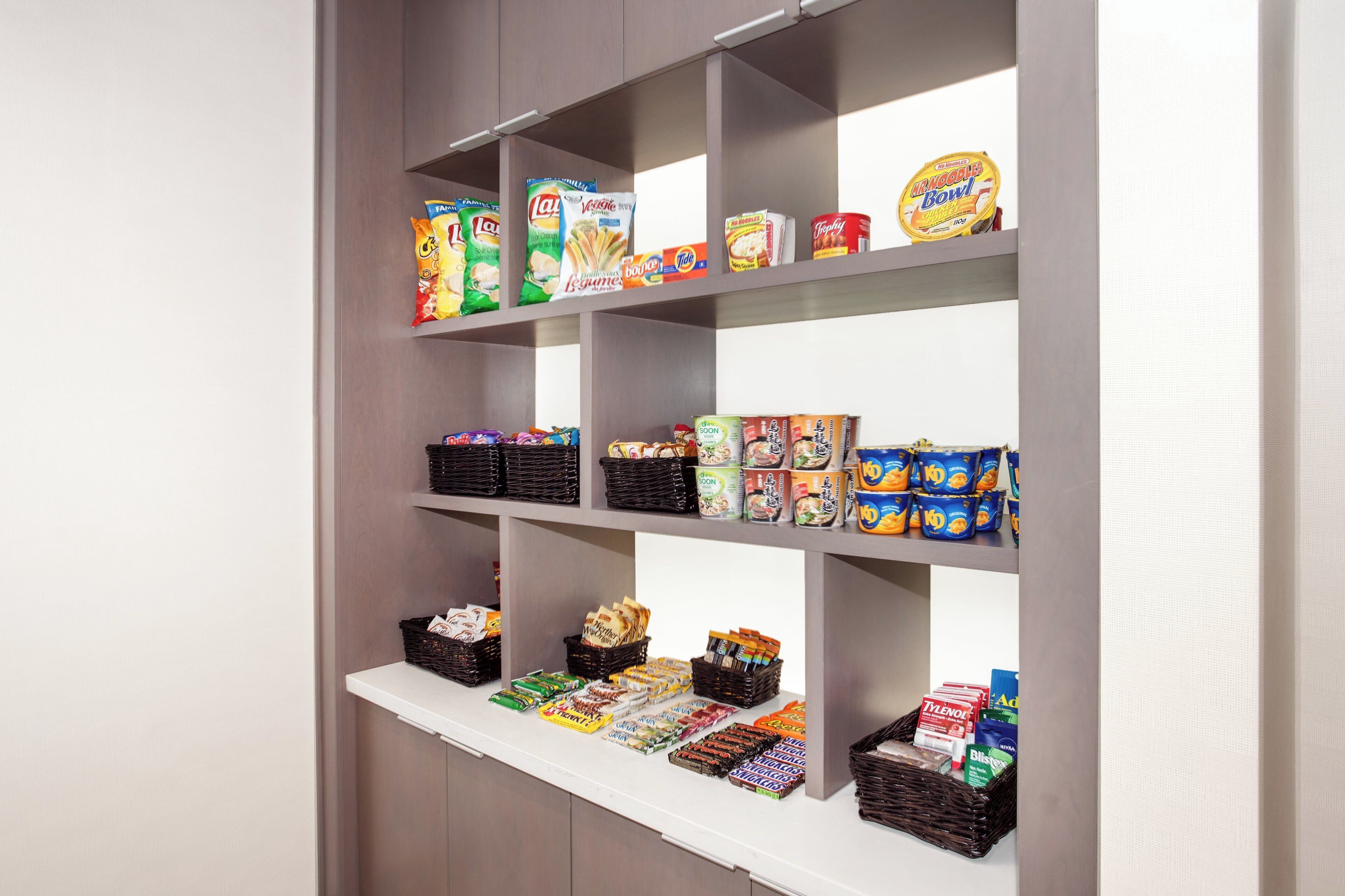 Una despensa con estantes llenos de diversos alimentos, entre ellos aperitivos, conservas y productos envasados.