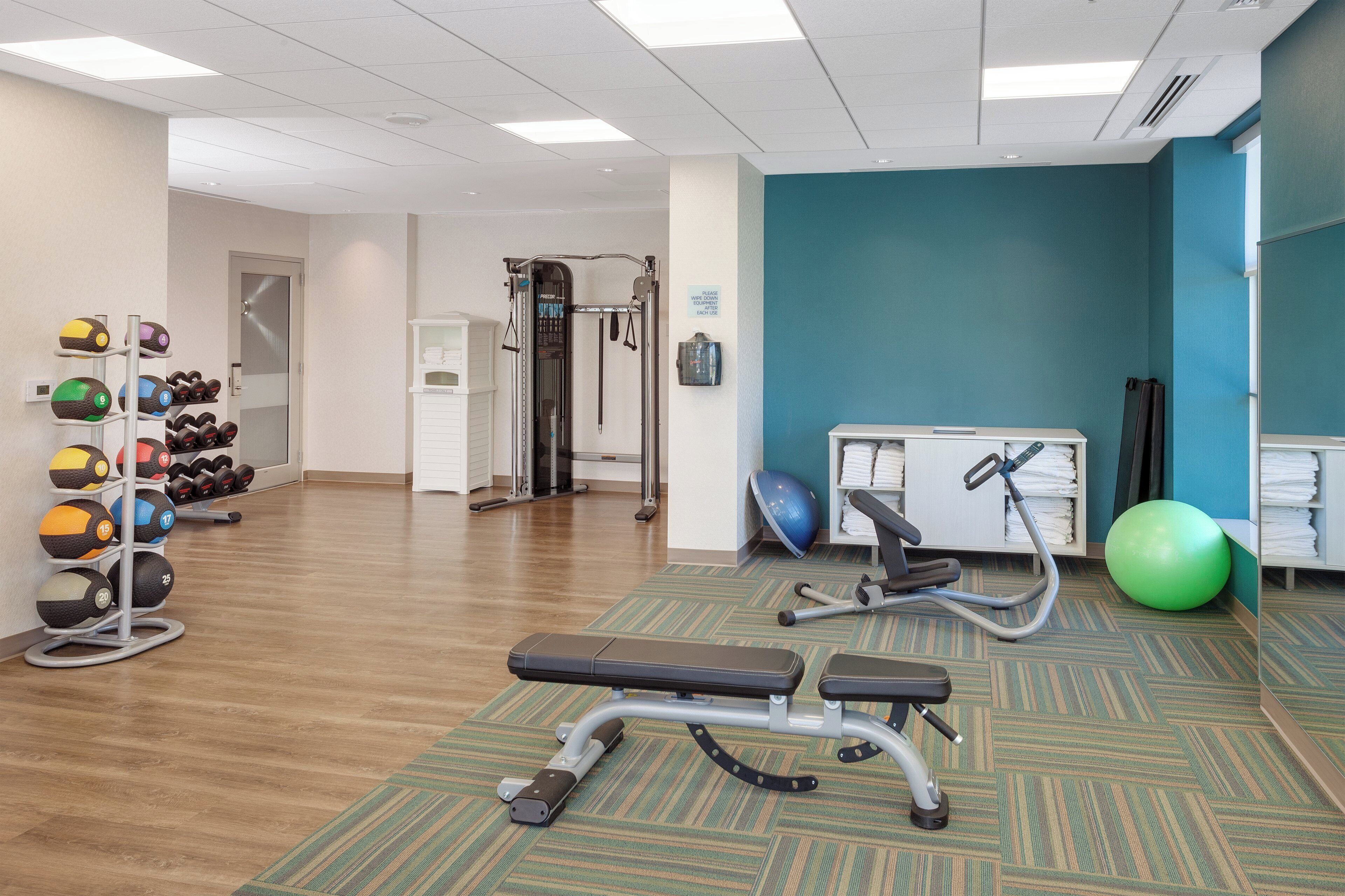 A gym with exercise equipment, a bench, and a wall-mounted rack of dumbbells.