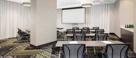 A conference room with a large table, chairs, a projector screen, and a carpeted floor.