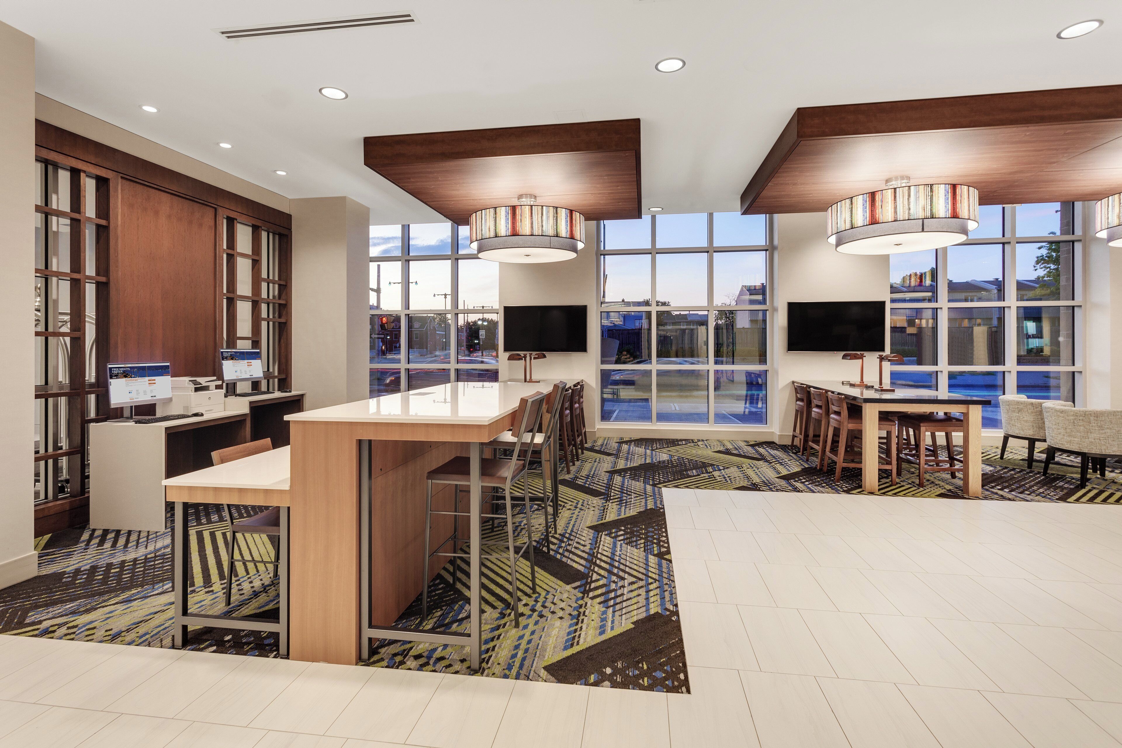 A modern hotel lobby with a reception desk, seating area, and large windows offering views of the outside.
